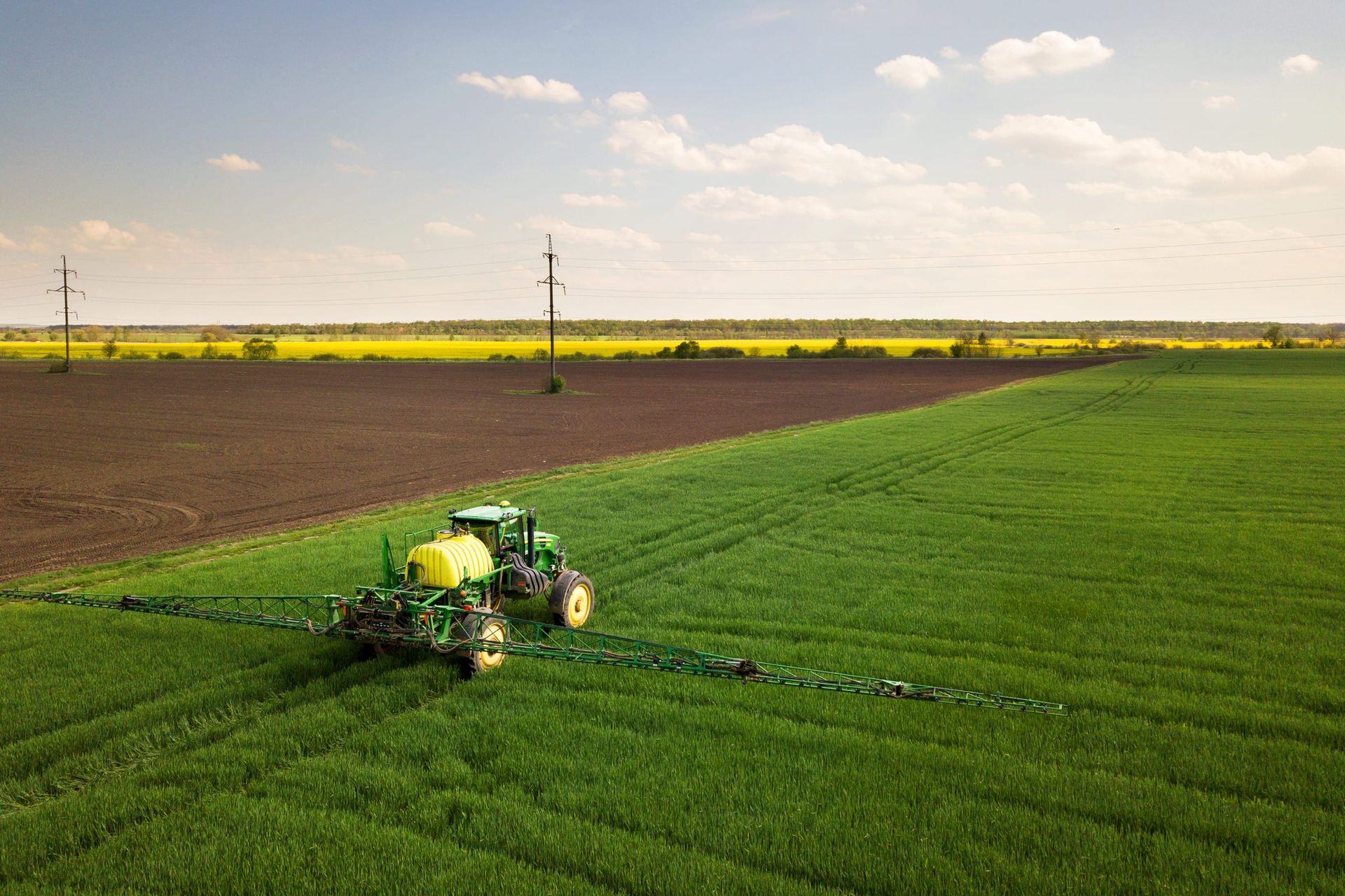 Tractor con depósito y barras pulverizadoras en un campo de cultivo